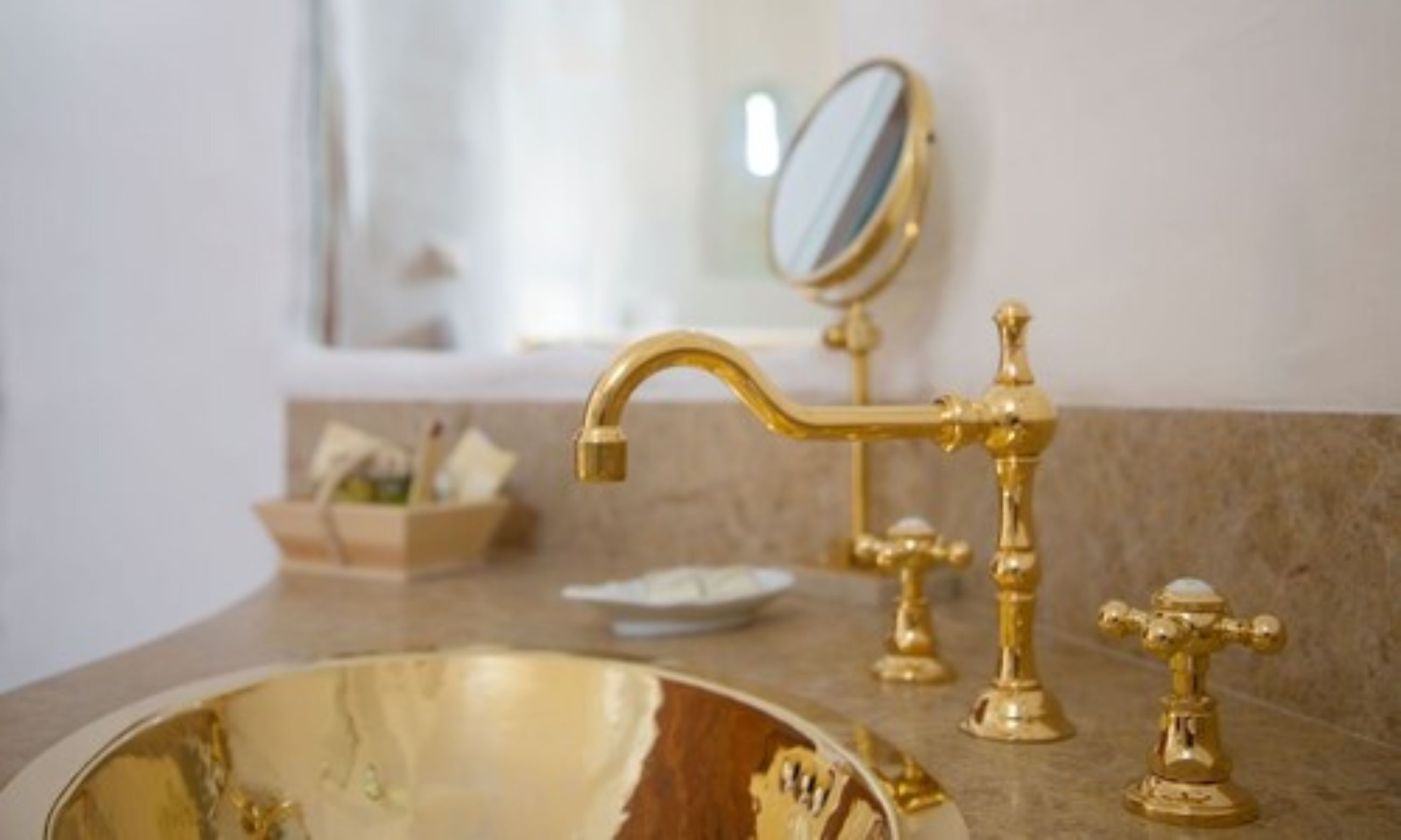 Un baño con un lavamanos dorado, un espejo y un perchero para toallas.