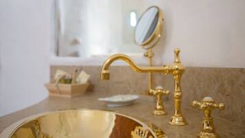 Un baño con un lavamanos dorado, un espejo y un perchero para toallas.