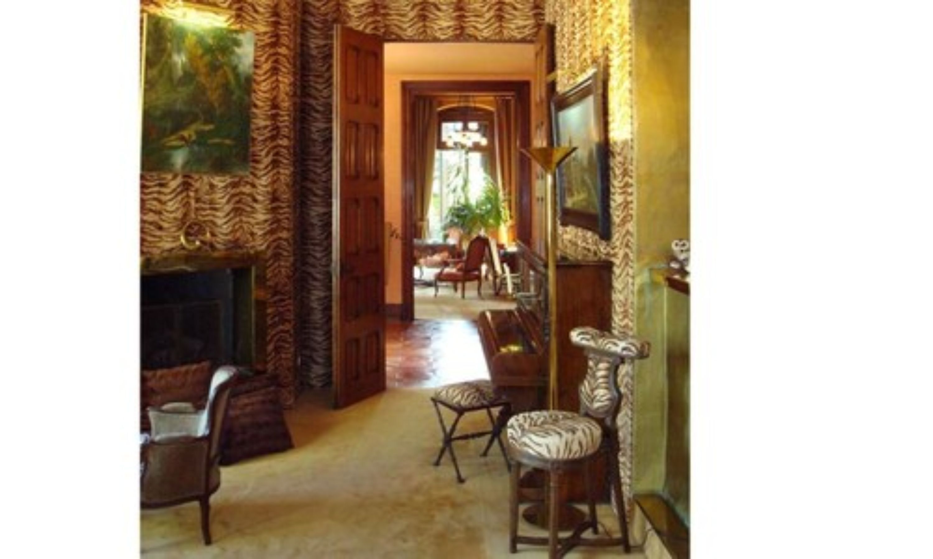 A room with a zebra-striped wallpaper, a fireplace, and a view of another room through an open door.