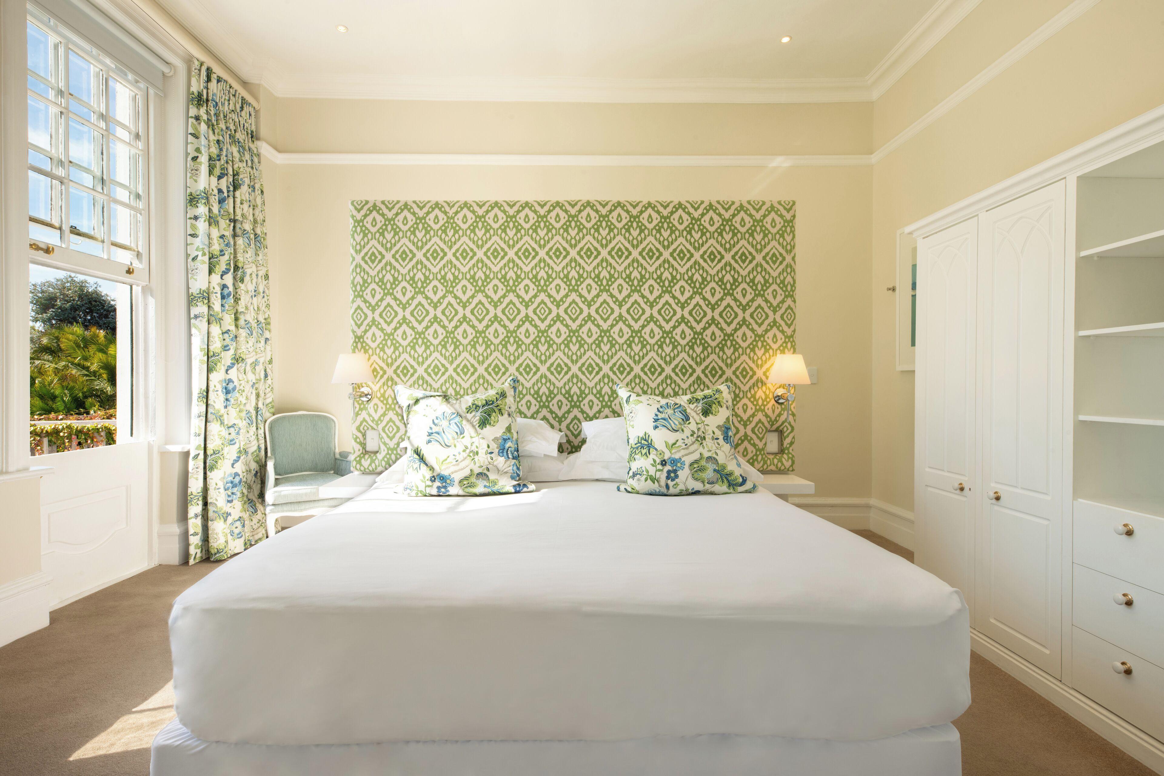 A bedroom with a large bed, two bedside lamps, a chair, and a wardrobe.