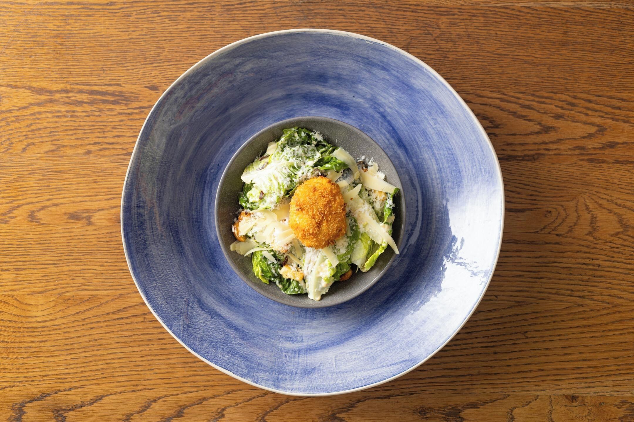 A blue ceramic bowl with a salad on a wooden table.