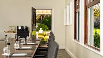 A conference room with a long table, chairs, and a view of a garden through the windows.