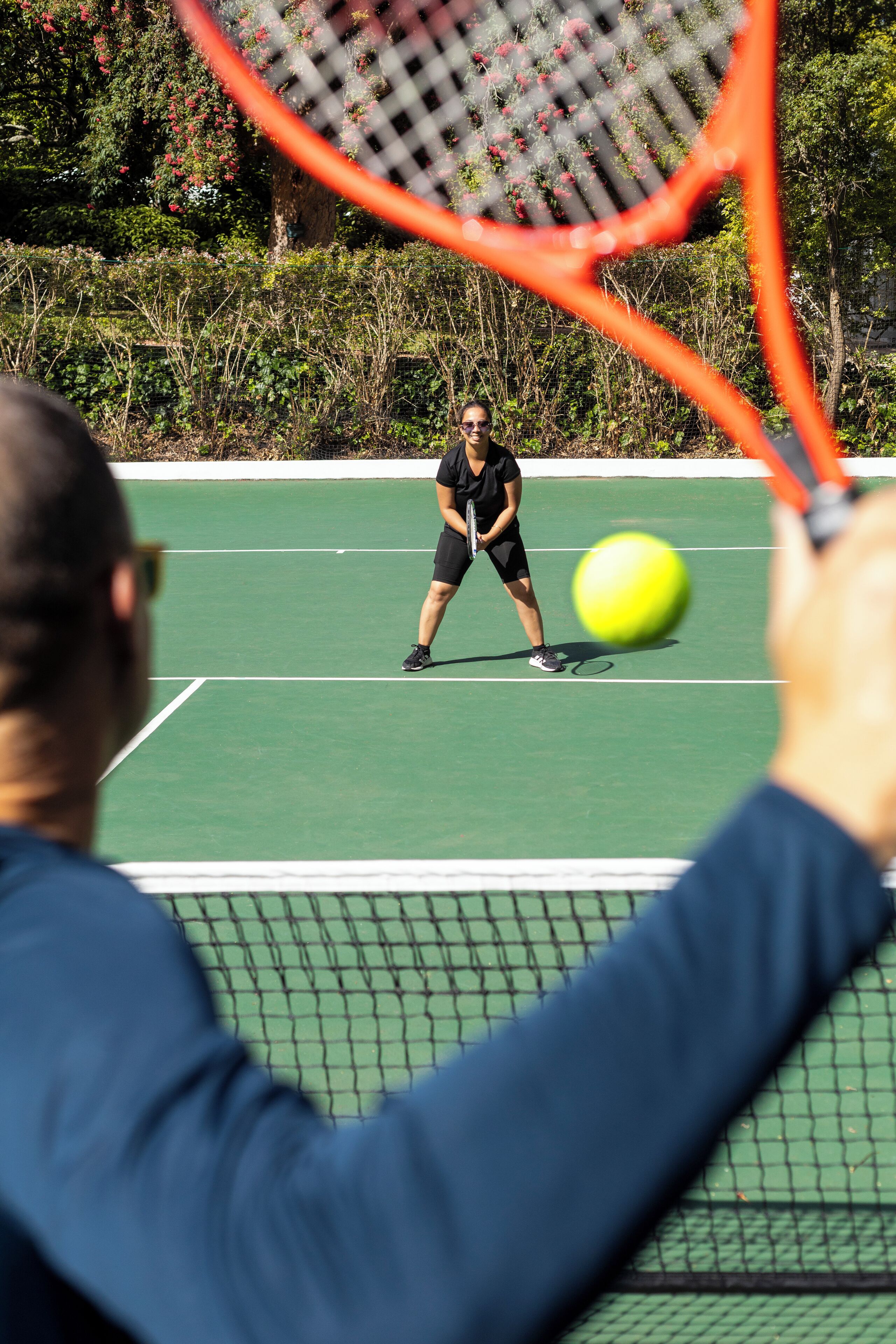 A tennis court with a net, a player in black attire, and a tennis ball in motion.