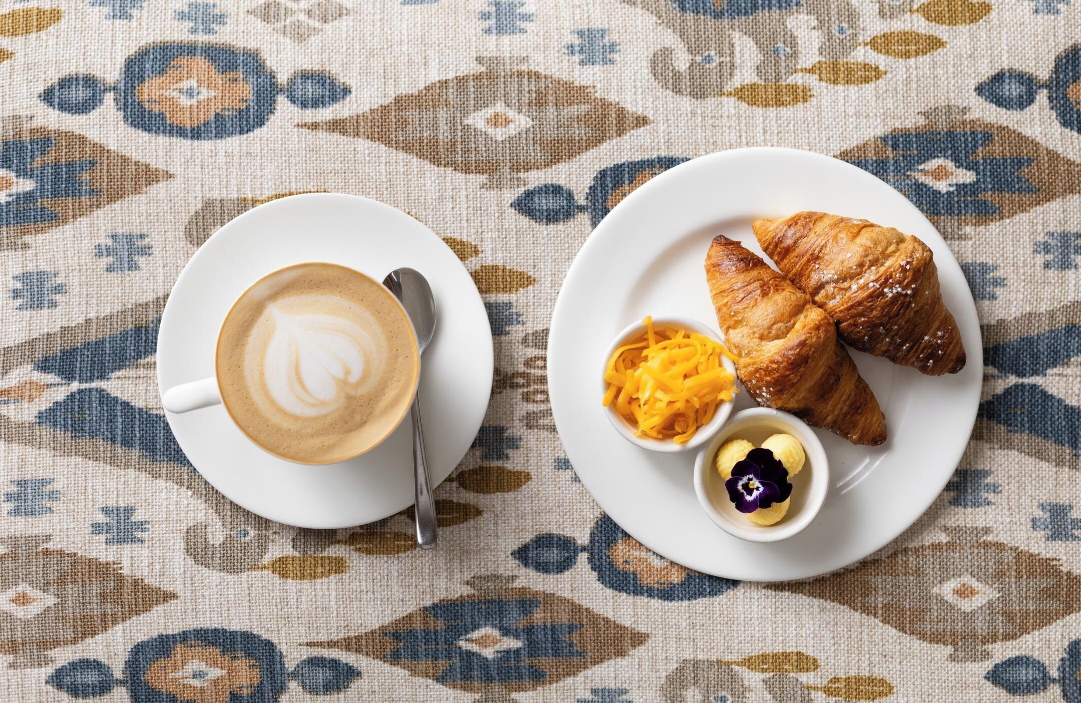 Une table avec une tasse de café et un croissant, le tout posé sur une nappe à motifs.