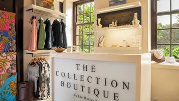A boutique with a display of clothes and accessories, a window with a view of greenery, and a sign reading "The Collection Boutique by Liz McGrath".