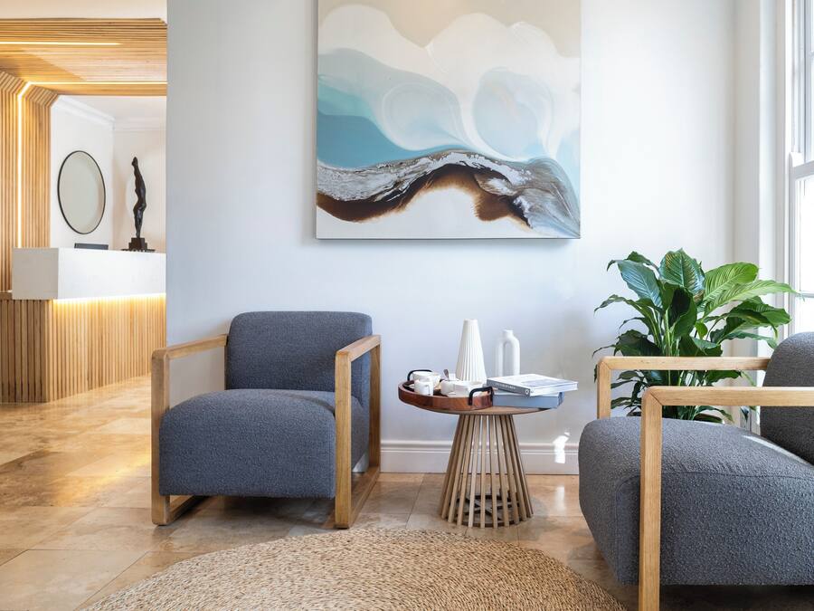 A modern lobby with a reception desk, a large abstract painting, and seating areas with a wooden floor and a woven rug.