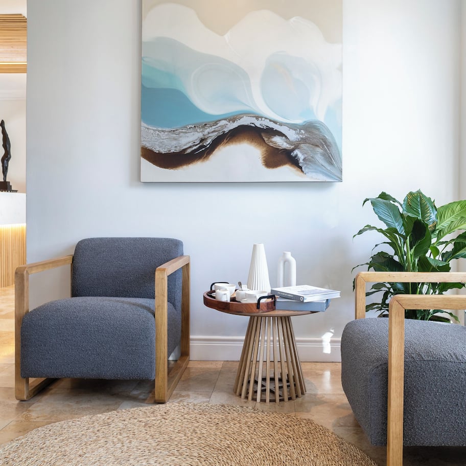 A modern lobby with a reception desk, a large abstract painting, and seating areas with a wooden floor and a woven rug.