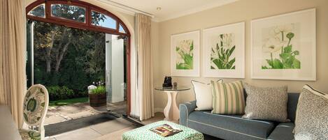 A living room with a sofa, ottoman, and chair, a coffee table, and framed botanical prints on the wall.