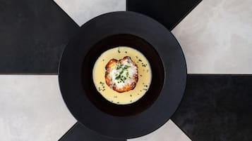 A black plate with a creamy dish and a piece of bread, set on a tiled floor with a geometric pattern.