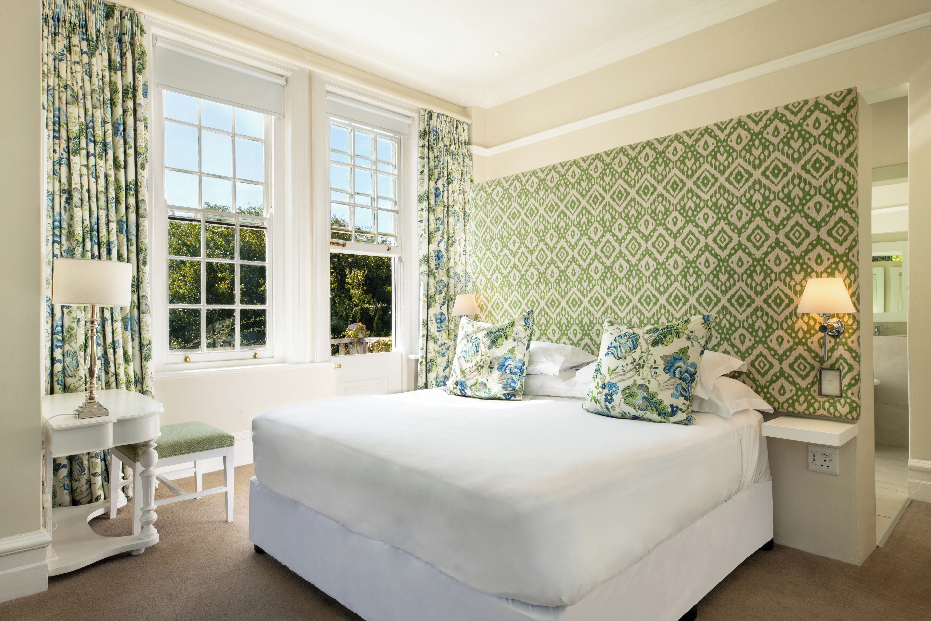 A bedroom with a large bed, a bedside table, a nightstand, and a window with curtains.