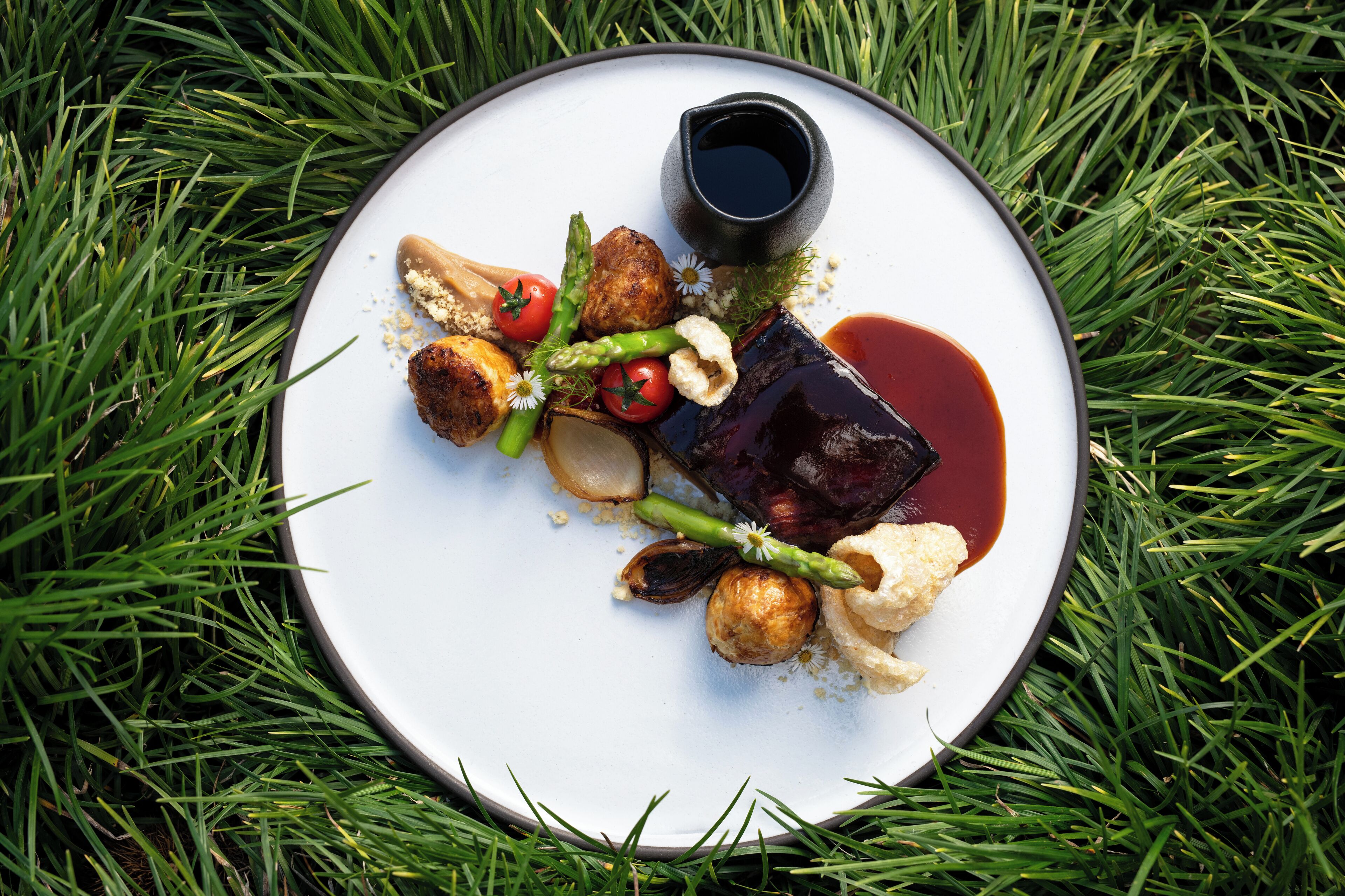 Un plato de comida con varias verduras y un recipiente pequeño de salsa, sobre césped.