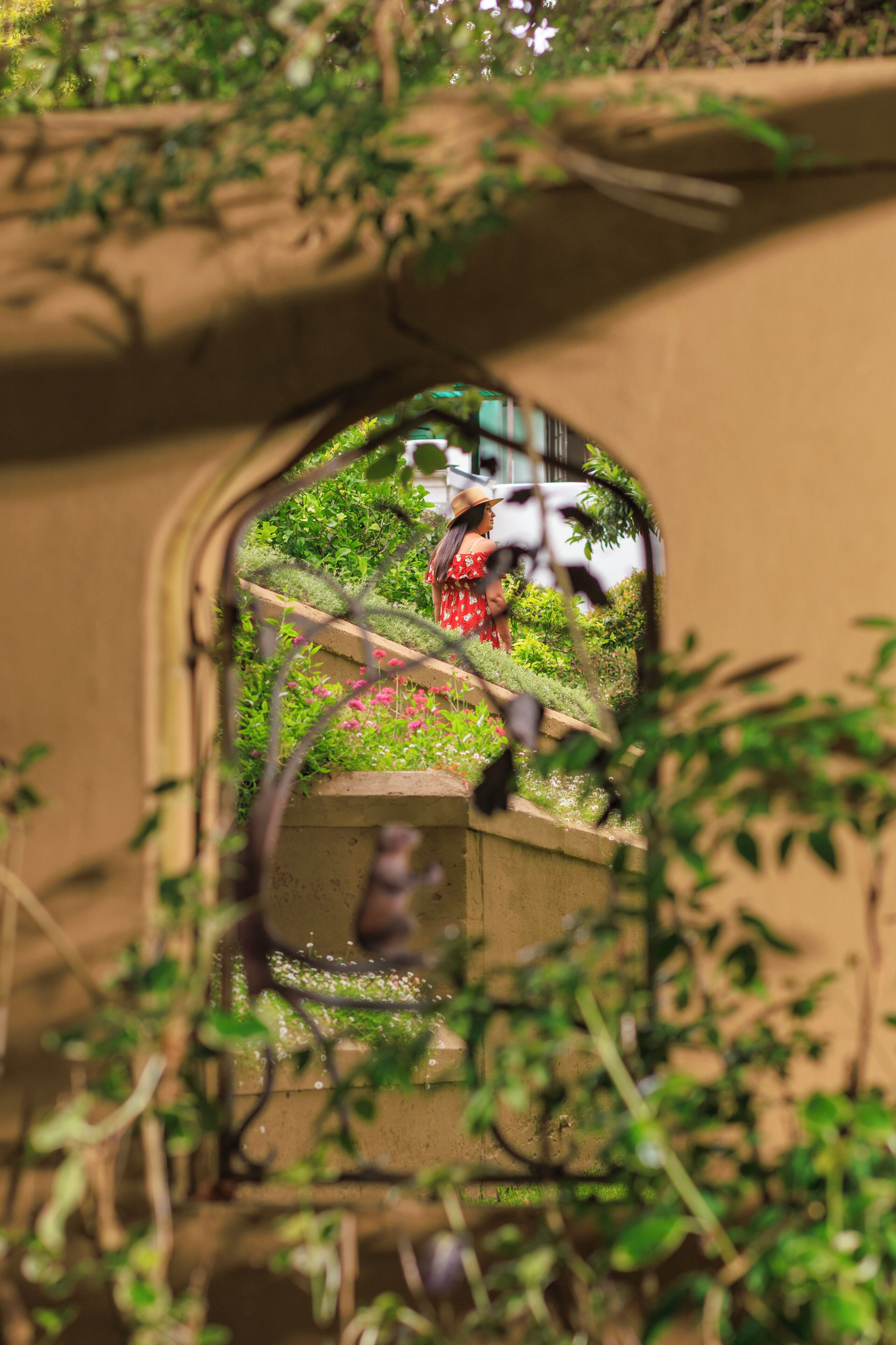 Blick durch ein Rundbogenfenster mit Grünpflanzen und einer Person in einem roten Kleid.