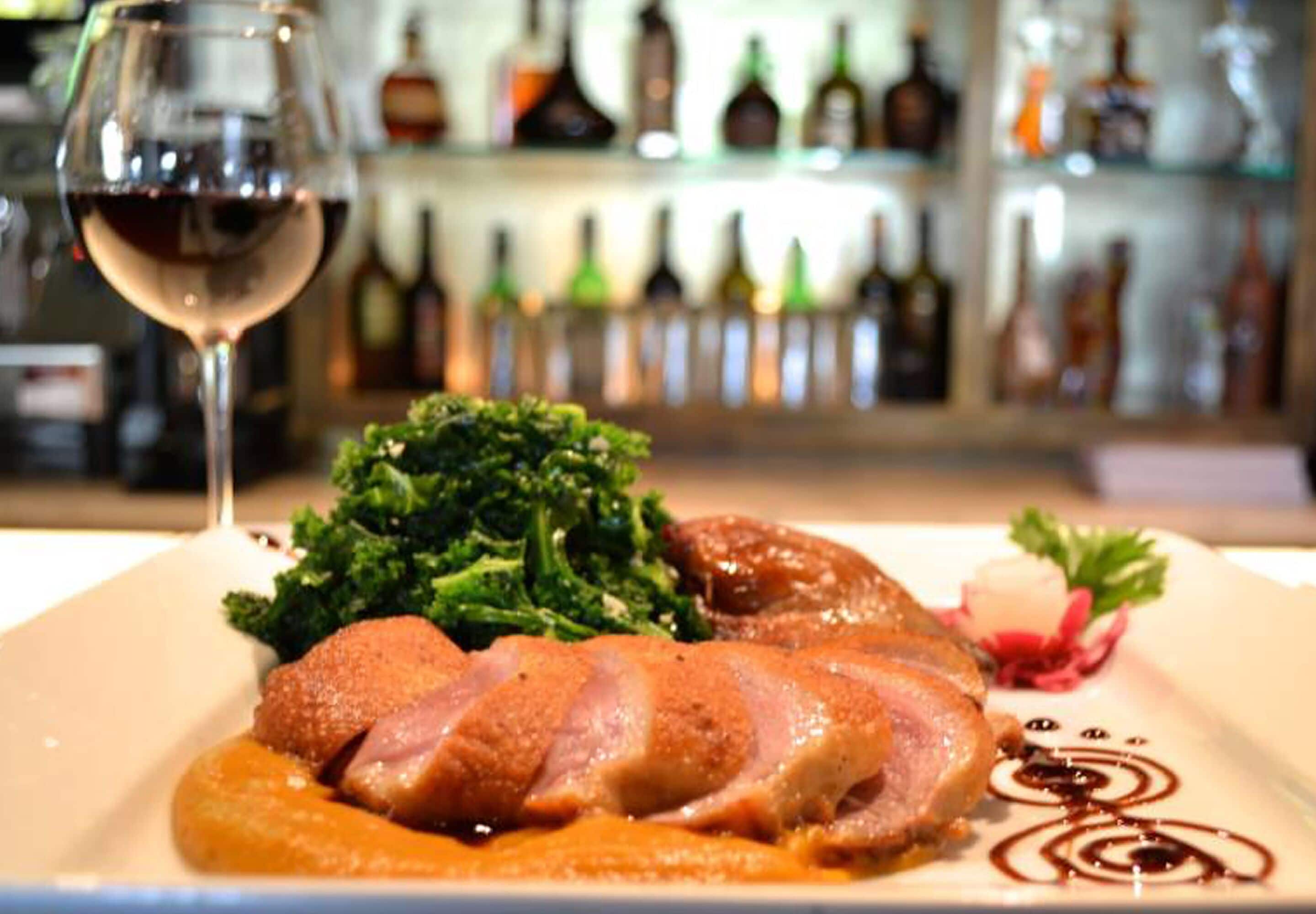 Un plato de comida con una copa de vino y una variedad de botellas al fondo.