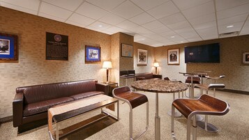 Un salón de conferencias con un sofá de cuero marrón, una mesa redonda y varias sillas. Se observan cuadros enmarcados y una placa en las paredes.