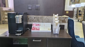 Una reception con una macchina del caffè, una piccola area salotto con una poltrona blu e un tappeto decorato.
