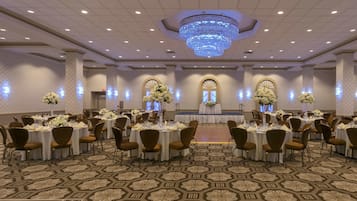 A banquet hall with round tables, chairs, and floral centerpieces.