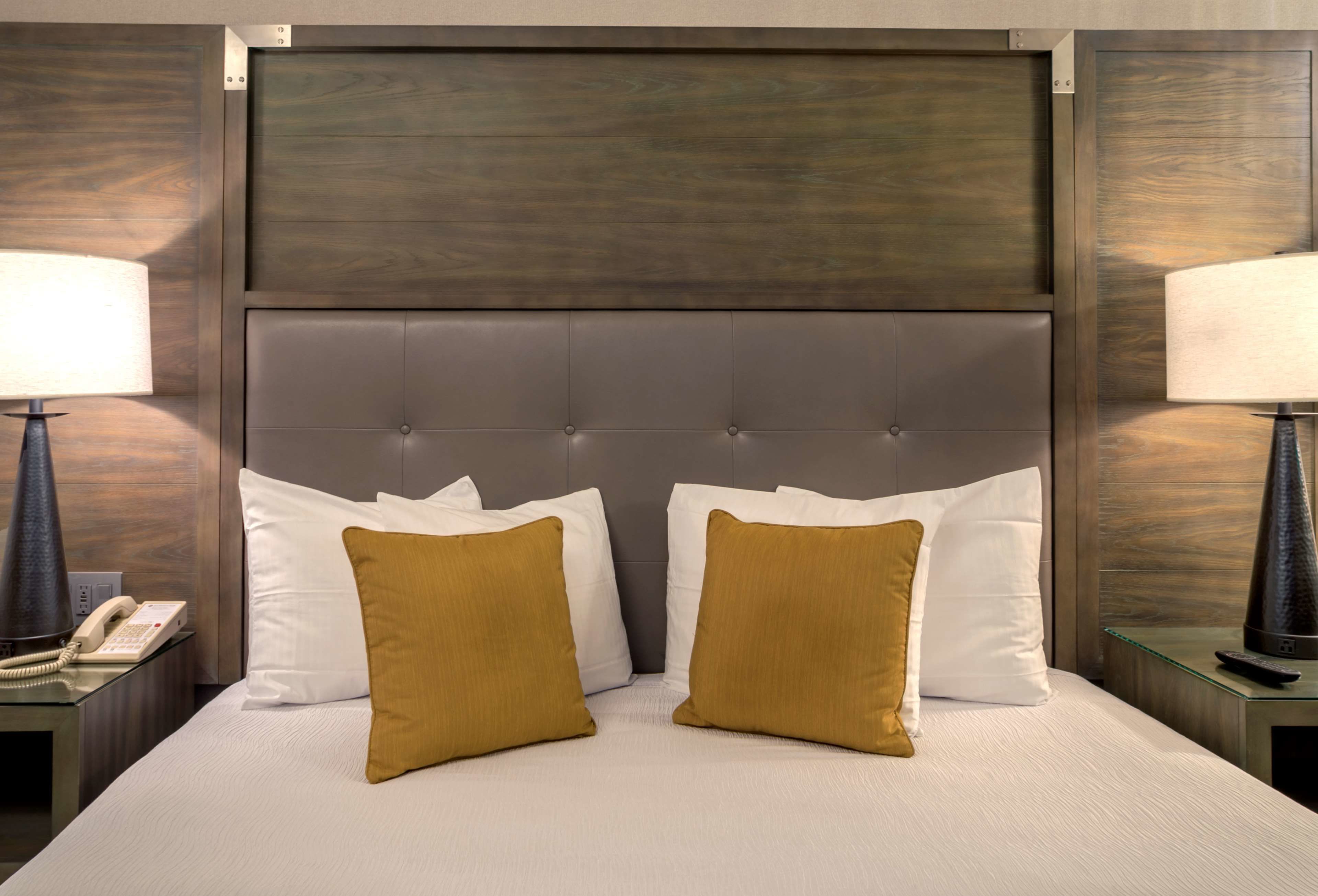 A hotel room with a large bed, two bedside lamps, a telephone, and a wooden headboard.