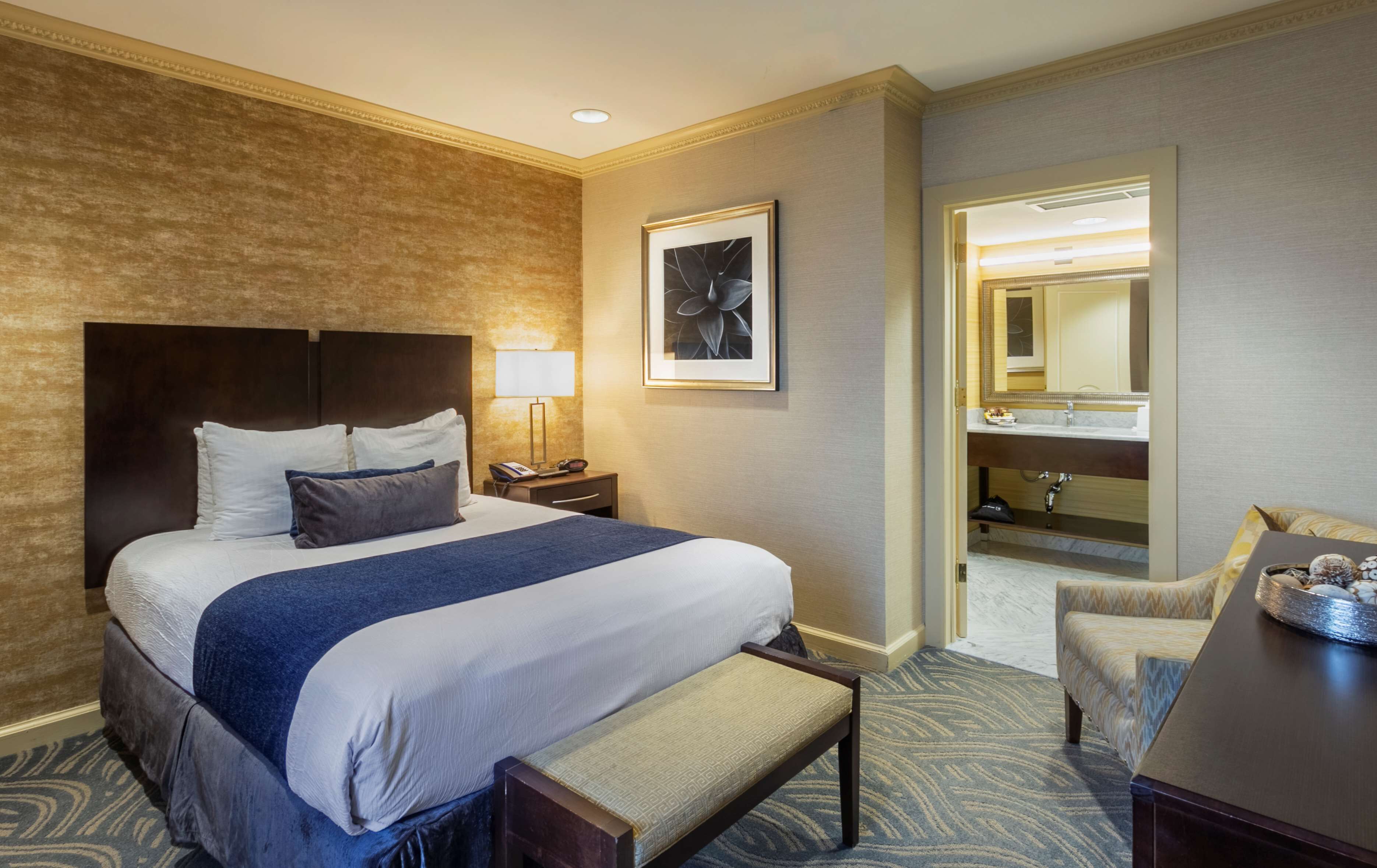 Habitación de hotel con una cama grande, mesita de noche, lámpara y un banco.