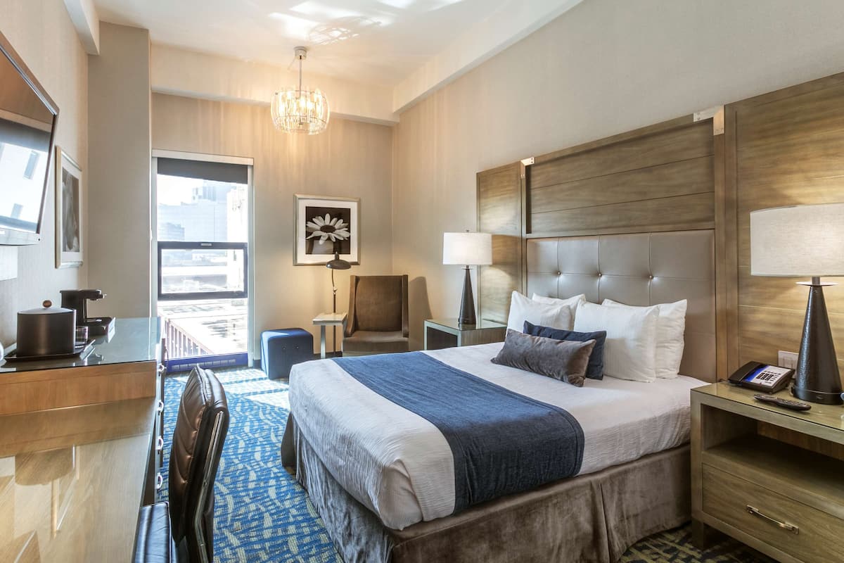 A hotel room with a large bed, a desk, a chair, a television, and a window with a city view.