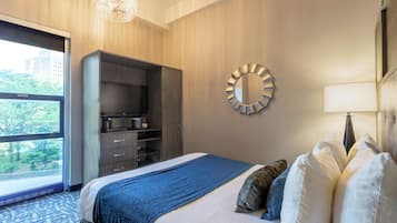 A hotel room with a large bed, a wardrobe, a round mirror, and a view of trees through a window.