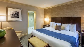 Una habitación de hotel con una cama grande, un escritorio, una silla, un cuadro en la pared y un baño visible a través de una puerta abierta.