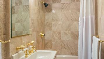 A bathroom with a marble-tiled shower, a white bathtub, and a sink with gold fixtures.