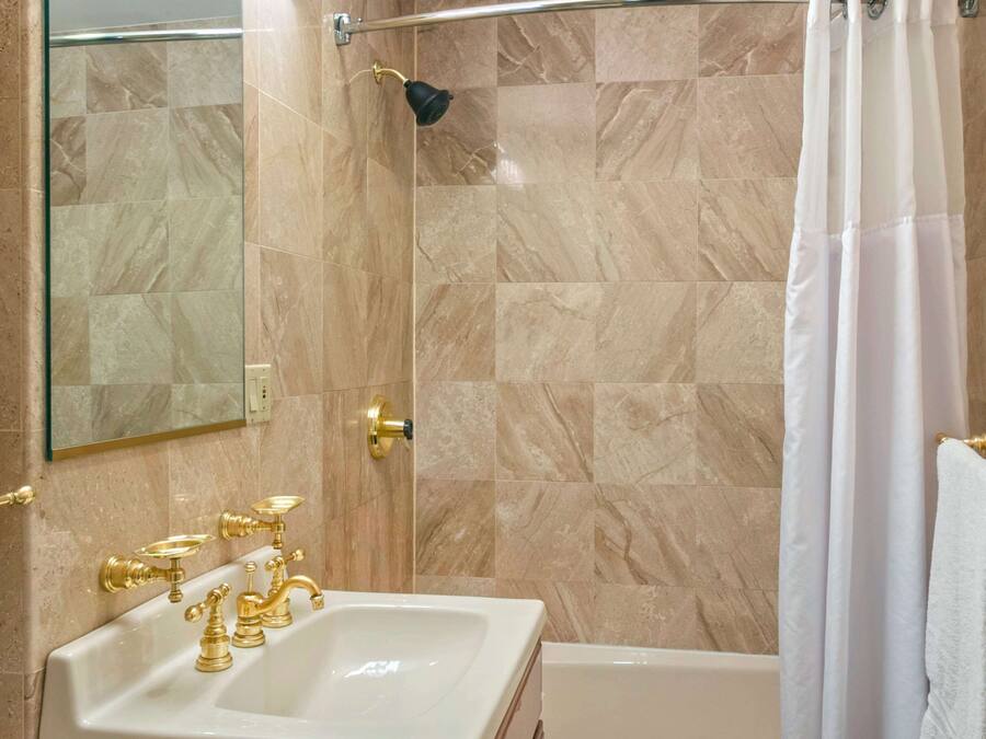 A bathroom with a marble-tiled shower, a white bathtub, and a sink with gold fixtures.