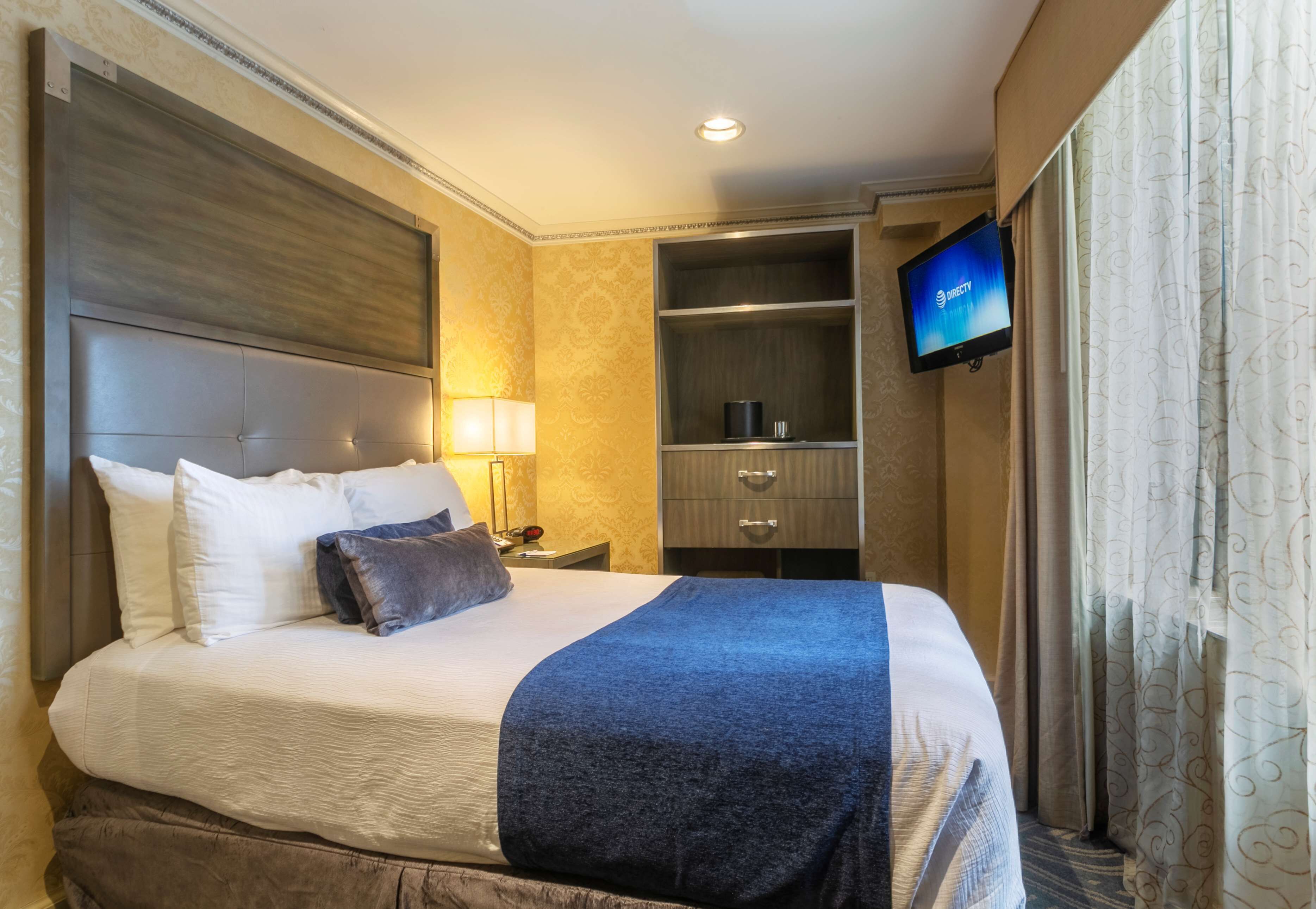 A hotel room with a large bed, a television mounted on the wall, a nightstand with a lamp, and a wardrobe.