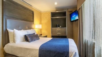 A hotel room with a large bed, a television mounted on the wall, a nightstand with a lamp, and a wardrobe.