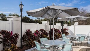 An outdoor patio with metal tables and chairs, large umbrellas, and a white fence. - Springhill Suites By Marriott Orlando Altamonte Springs (Altamonte Springs)