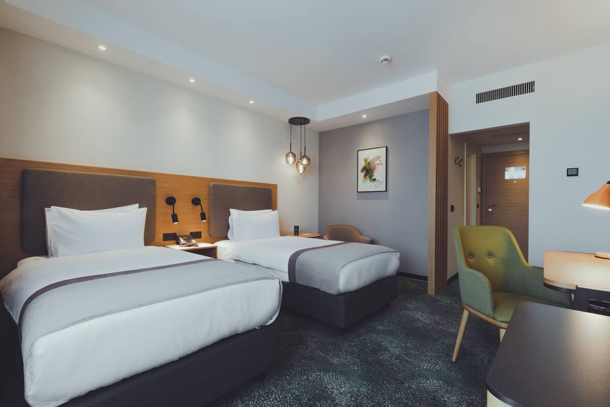 A hotel room with two beds, a desk, a chair, and a door leading to another room.