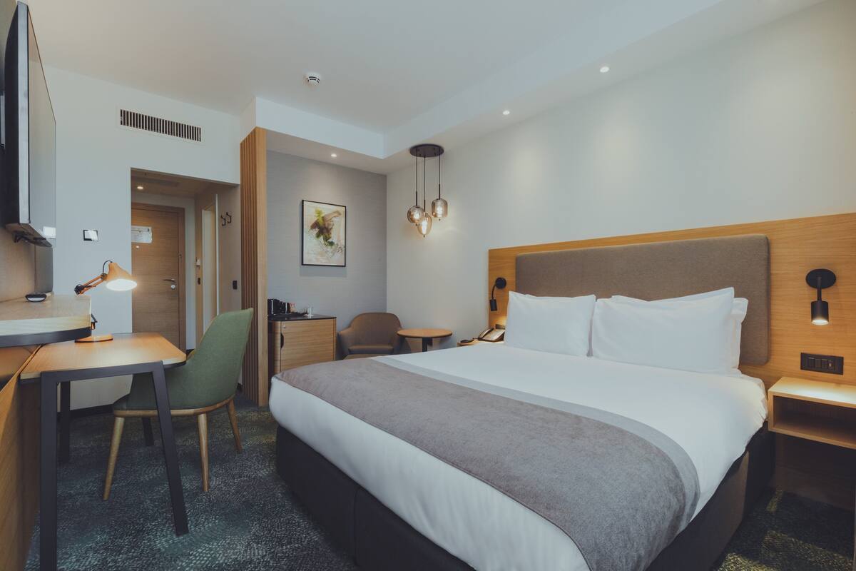A hotel room with a large bed, a desk with a chair, a small table, and a TV.