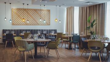 Un comedor moderno con mesas de madera, sillas tapizadas y lámparas colgantes.
