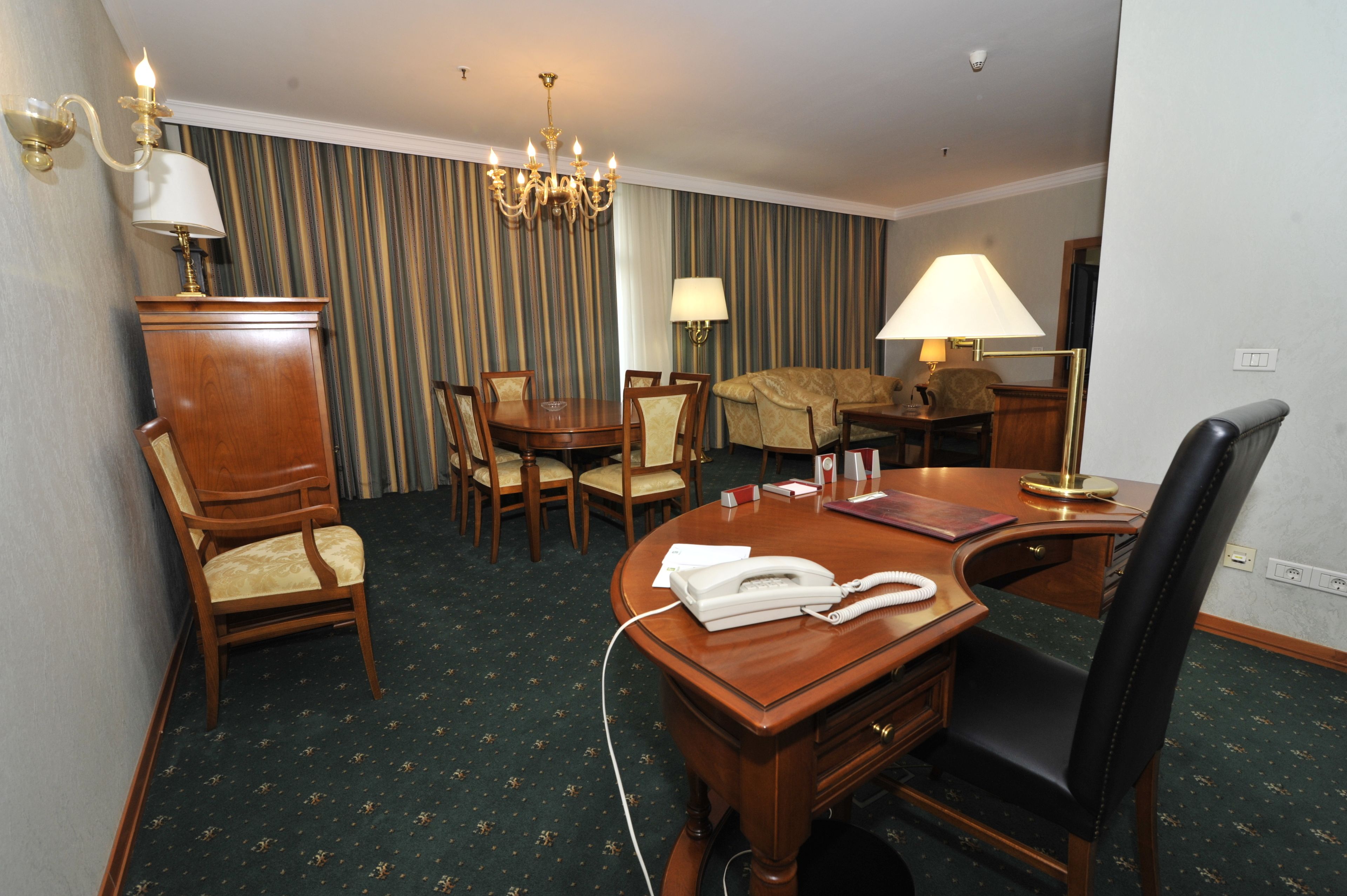 Ein Hotelzimmer mit Esstisch, Stühlen, einer Couch, einer Lampe, einem Telefon und Teppichboden.