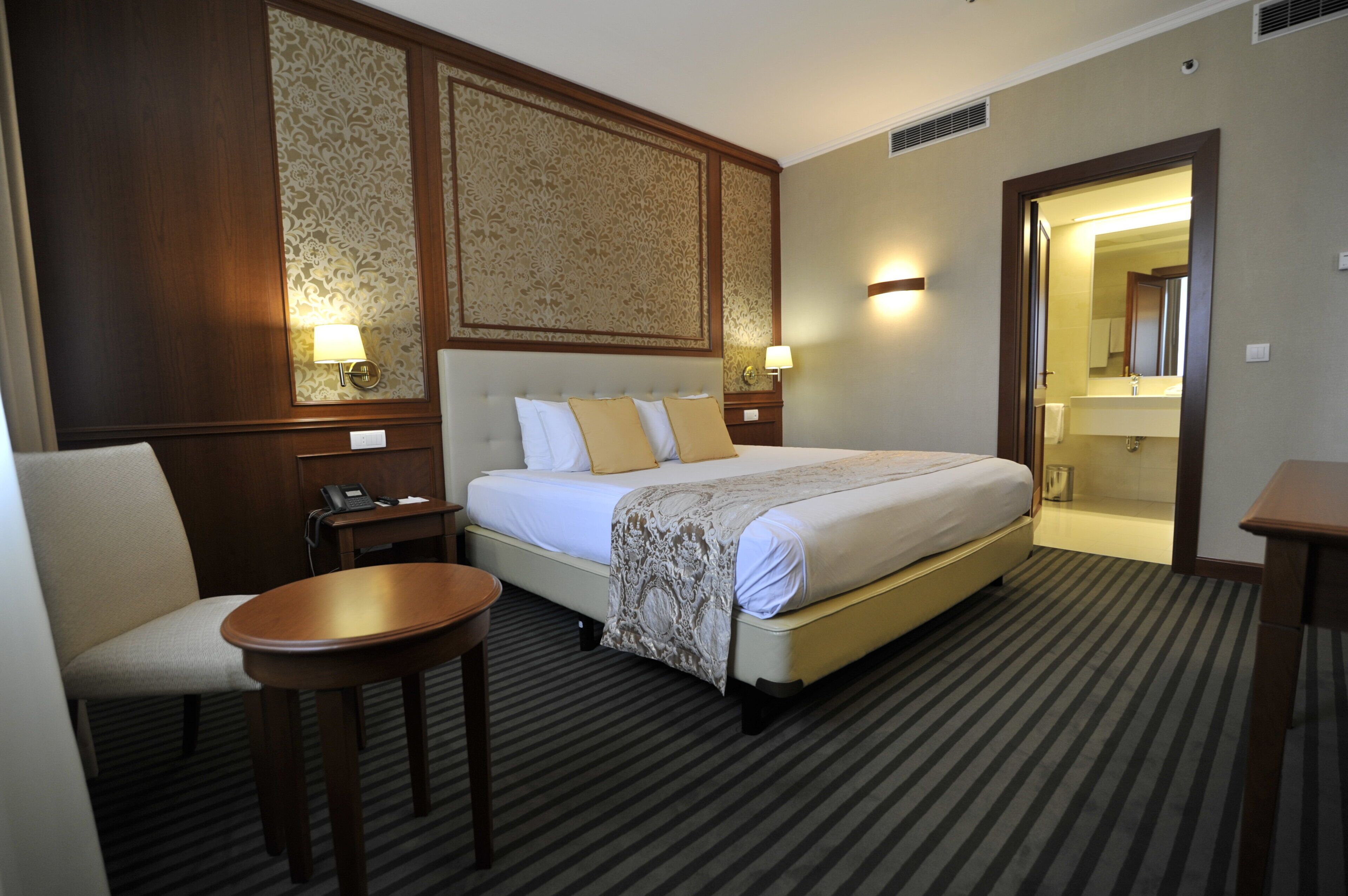 A hotel room with a large bed, a bedside table, a chair, and a bathroom visible through an open door.