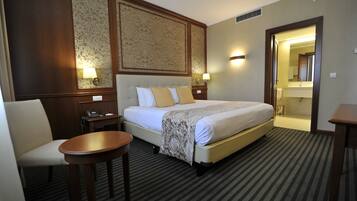 Habitación de hotel con una cama grande, una mesita de noche, una silla y un baño visible a través de una puerta abierta.