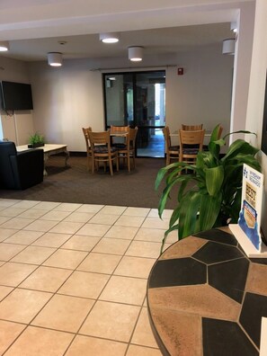 A lobby area with a reception desk, several wooden chairs, a tiled floor, and a potted plant.