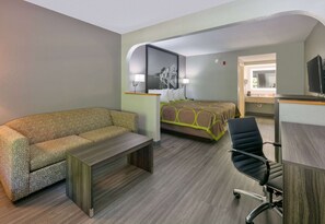 Habitación de hotel con sofá, cama con cubrecama de estampado verde y marrón, escritorio con silla y televisión.