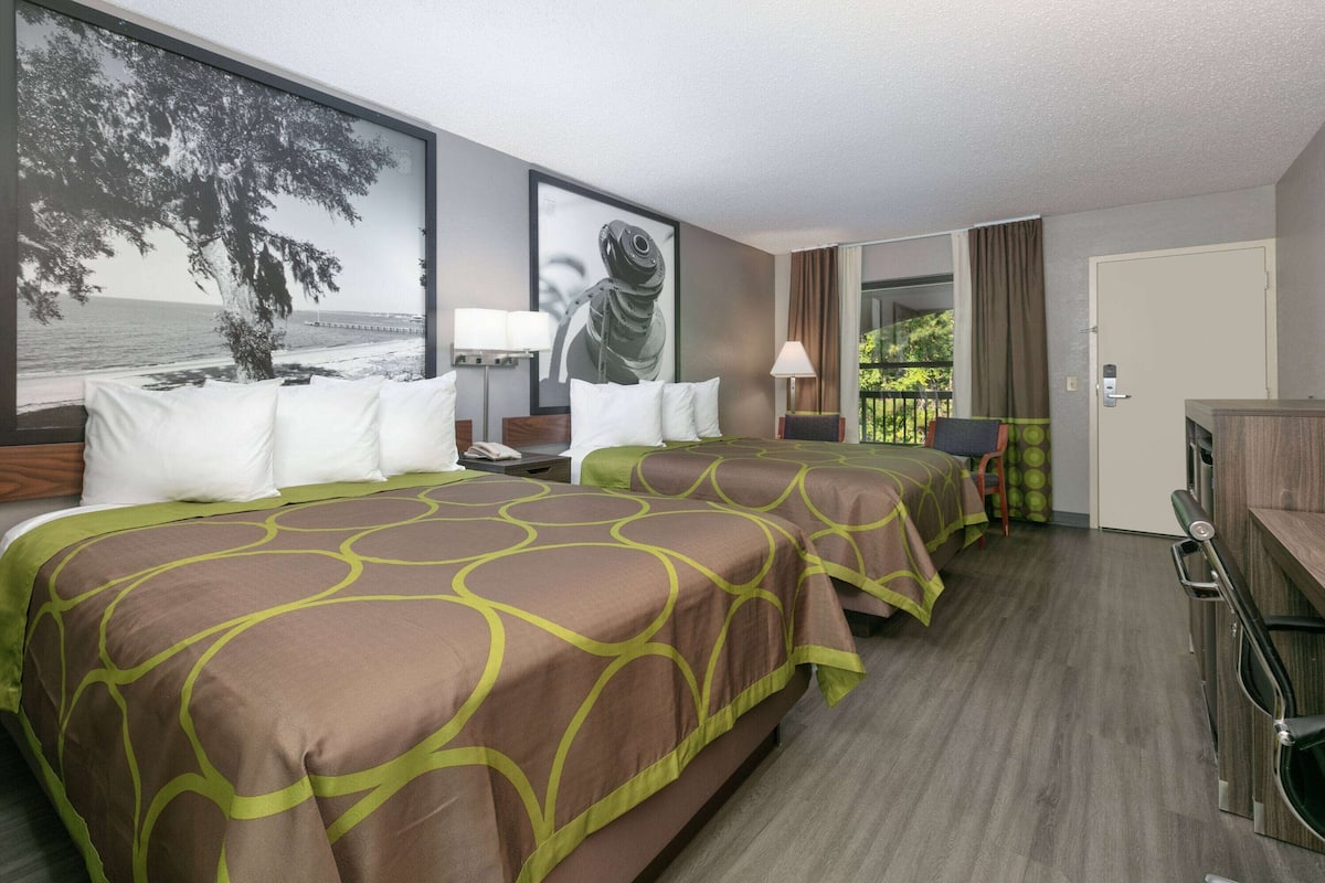 Quarto de hotel com duas camas, uma janela grande com vista para o mar, um quadro na parede e uma porta que dá para uma varanda.