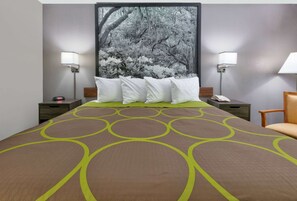 Habitación de hotel con una cama grande, dos mesitas de noche, una silla y una lámpara de pared.