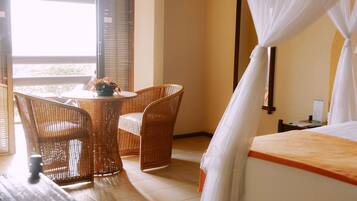 A hotel room with a bed, a small table with chairs, and a window with blinds.