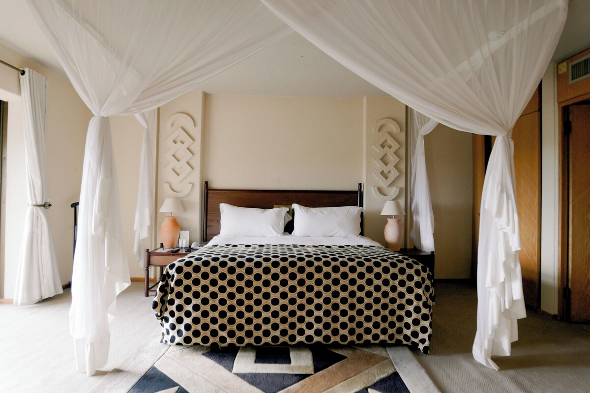 A bedroom with a bed under a canopy, a nightstand with a lamp, and a patterned bedspread.