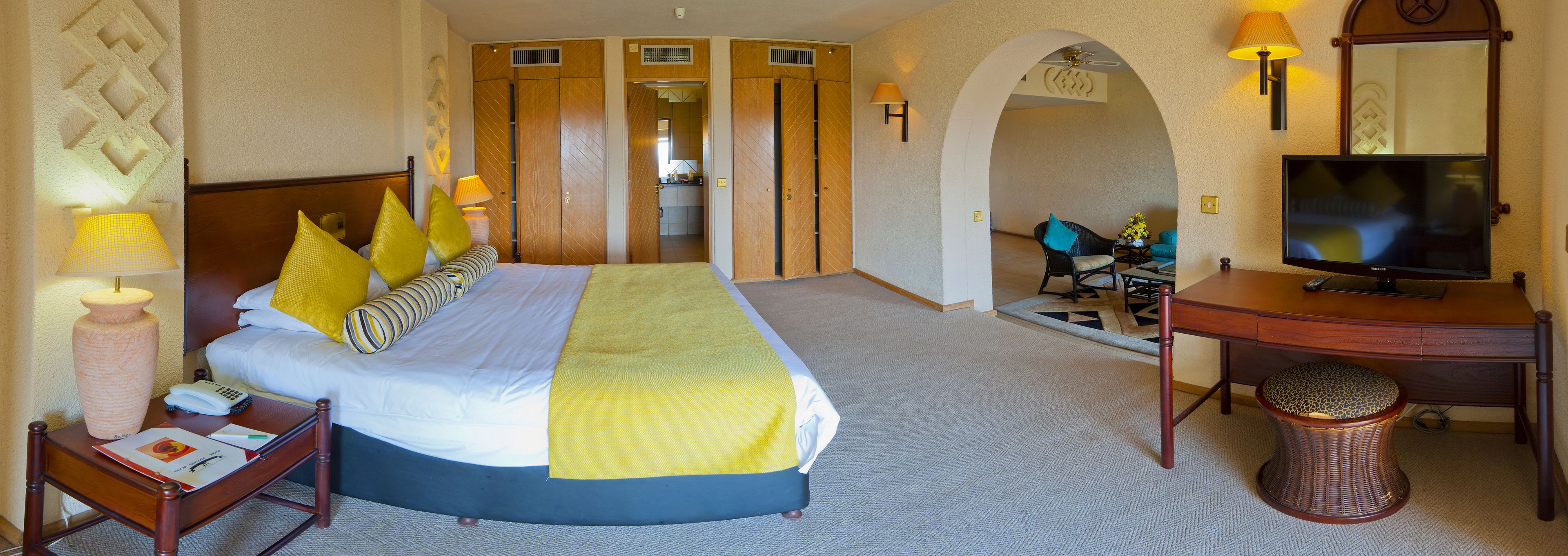 A hotel room with a large bed, a desk with a television, a chair, and a lamp.