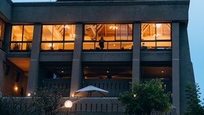 A multi-story building with large windows, a balcony, and outdoor seating with an umbrella. - Elephant Hills Resort (Victoria Falls)