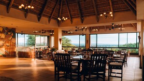 A spacious dining area with high ceilings and large windows offering a view of the landscape. - Elephant Hills Resort (Victoria Falls)