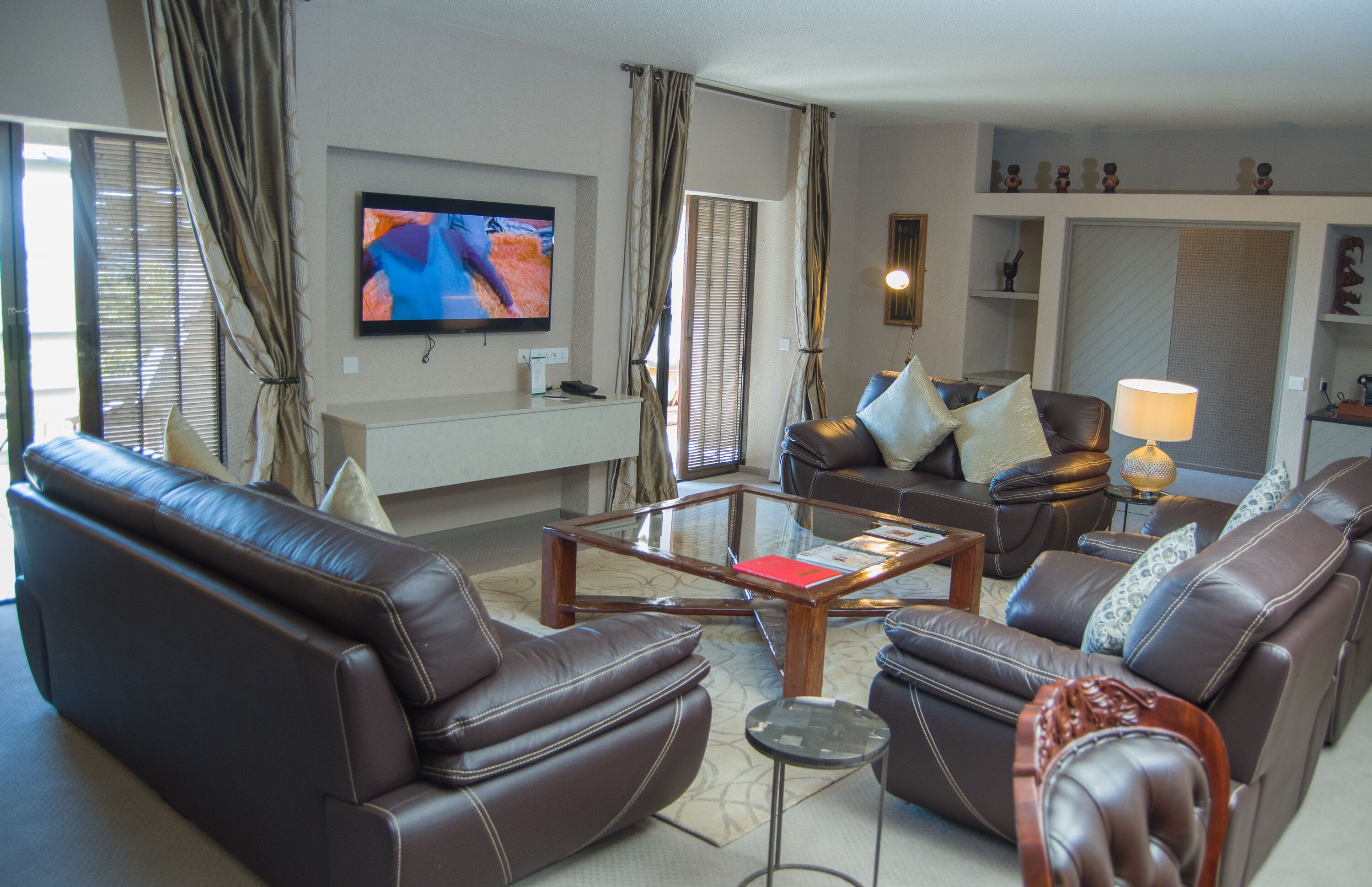 A living room with leather sofas, a glass coffee table, and a flat-screen TV mounted on the wall.