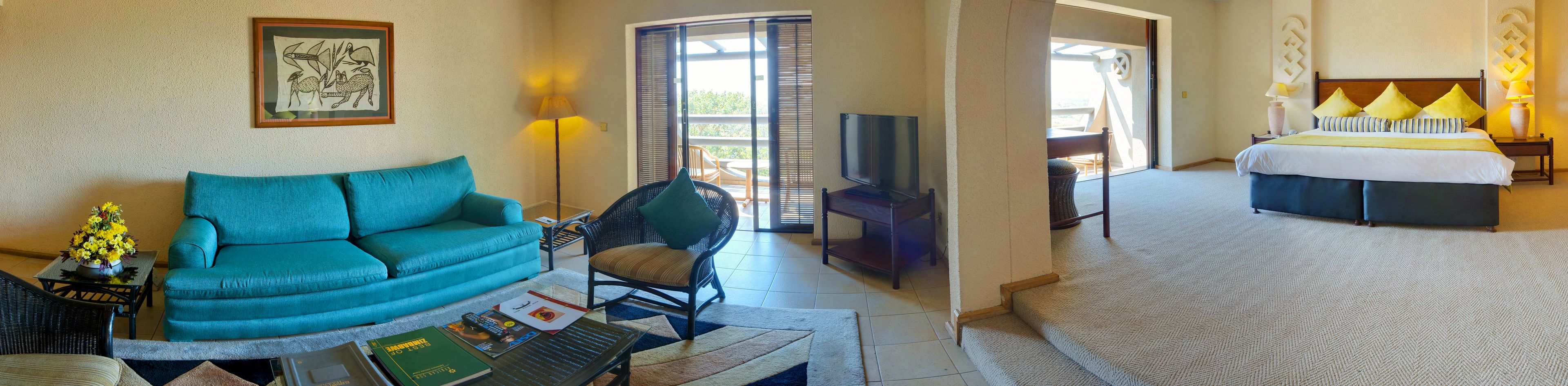 A hotel room with a sofa, armchair, TV, bed, and a view of the outdoors.