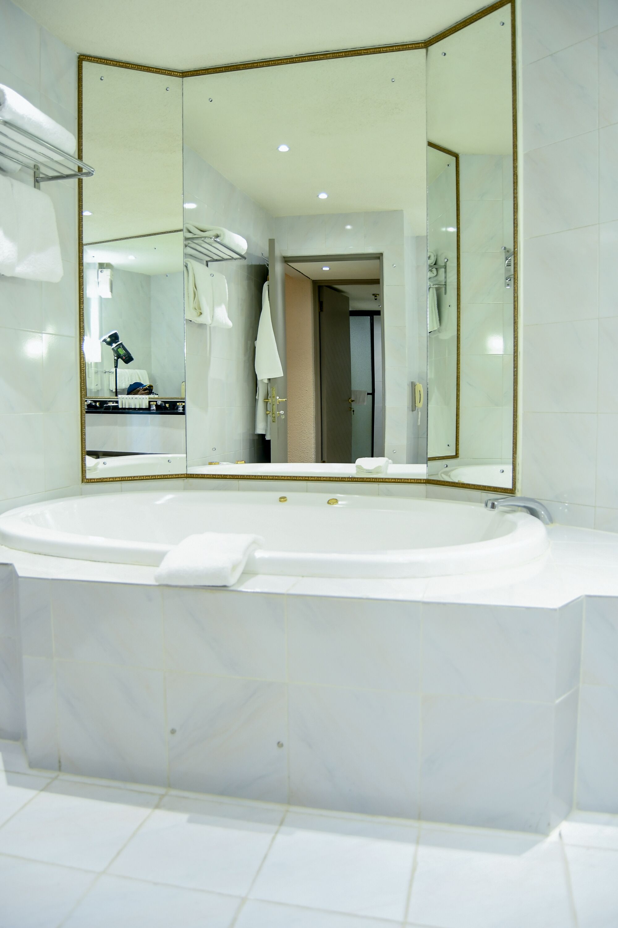 A modern bathroom with a large freestanding bathtub, a large mirror with a gold frame, and a towel rack.