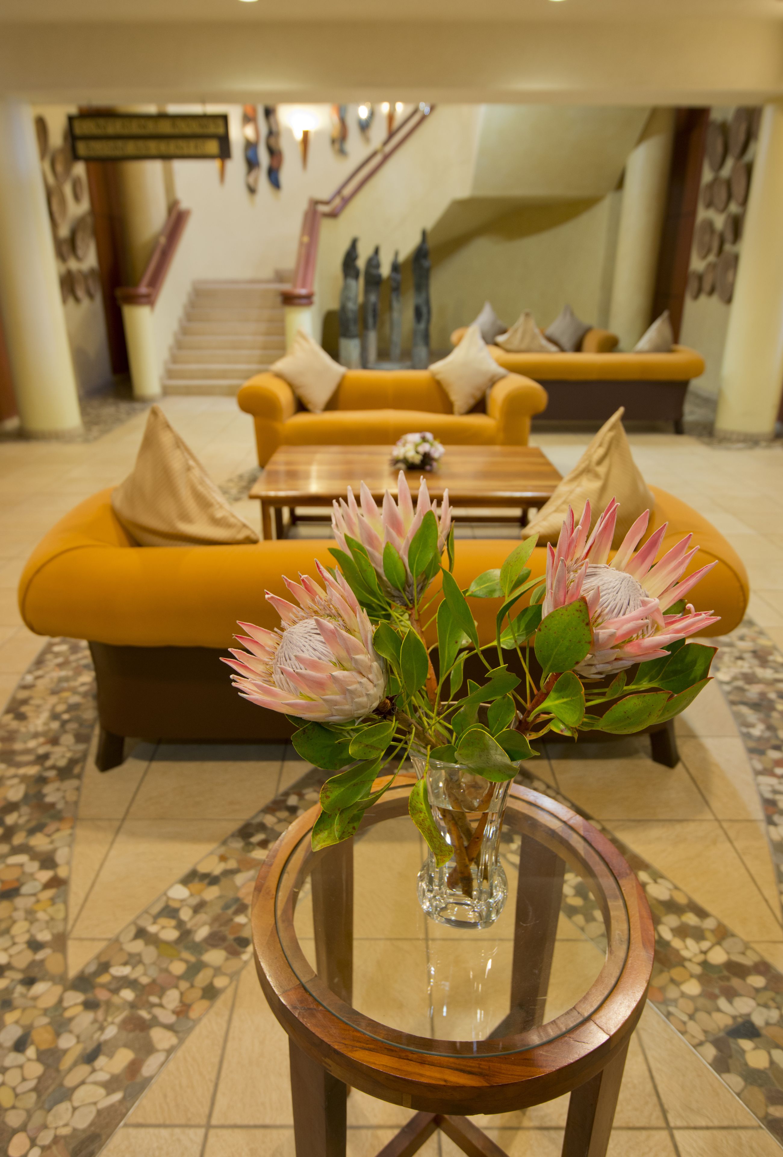 A lobby with a round glass table, a yellow sofa, and a staircase in the background.