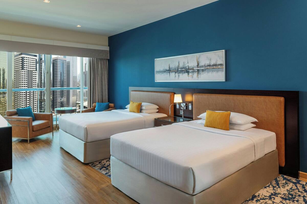 A hotel room with two beds, a desk, and a chair.